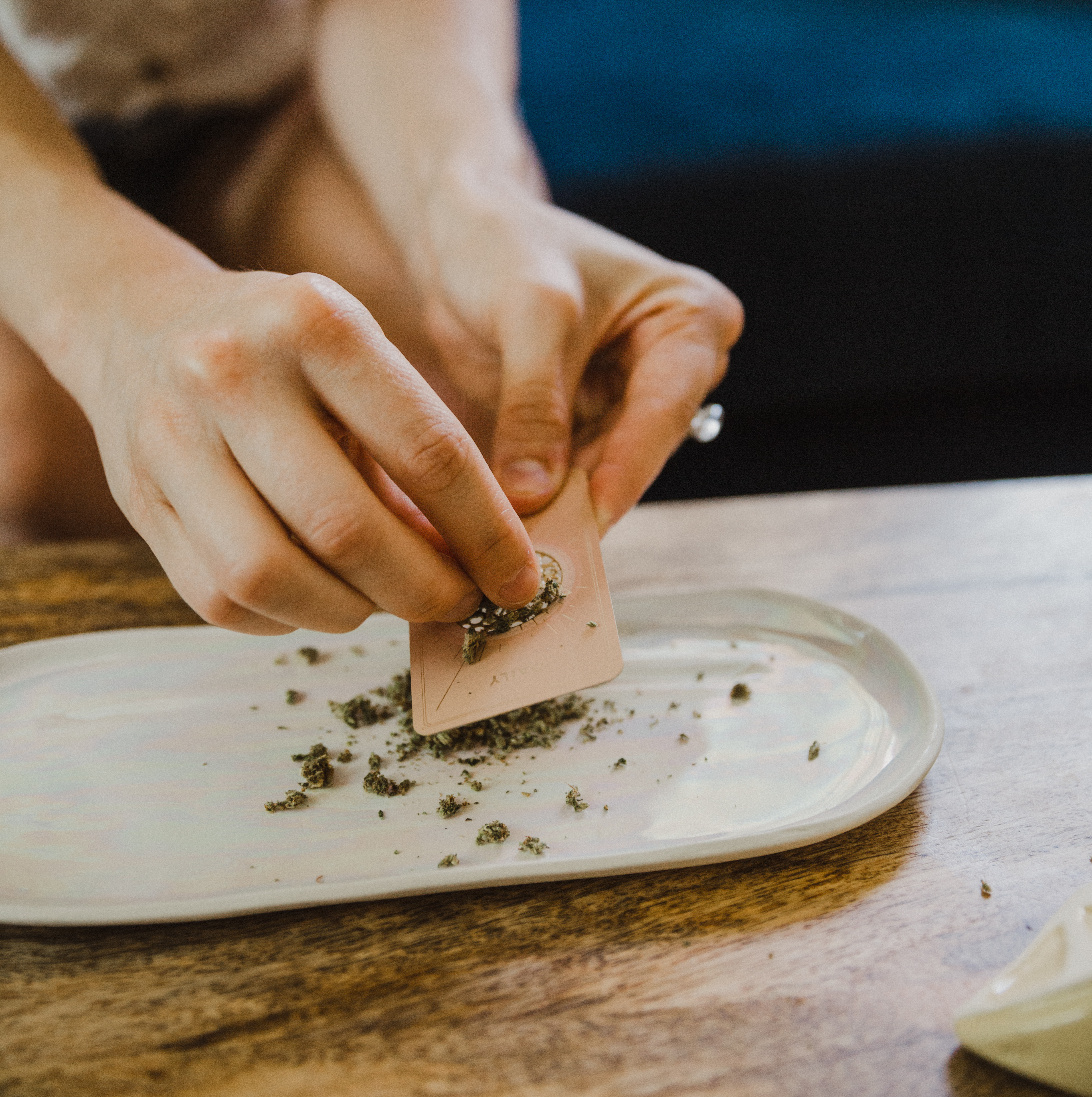 Hand-grinding cannabis onto Wandering Bud ceramic rolling tray in pearl